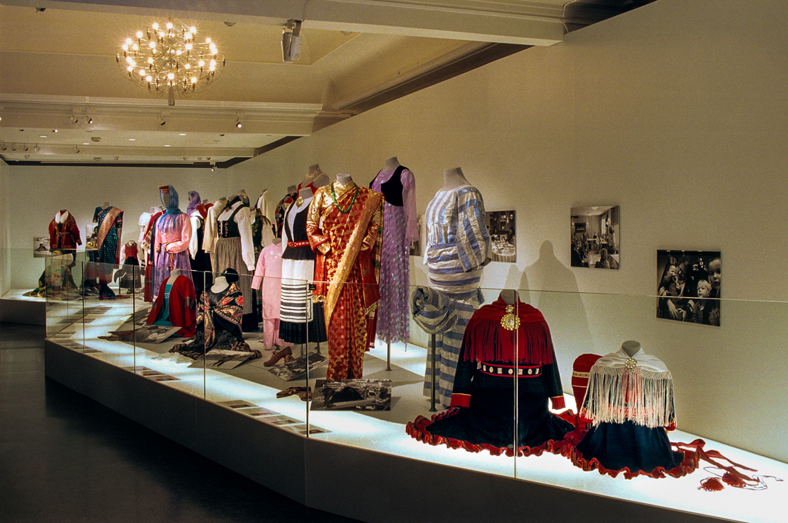 Exhibition room with many folk costumes displayed on a podium. Photo