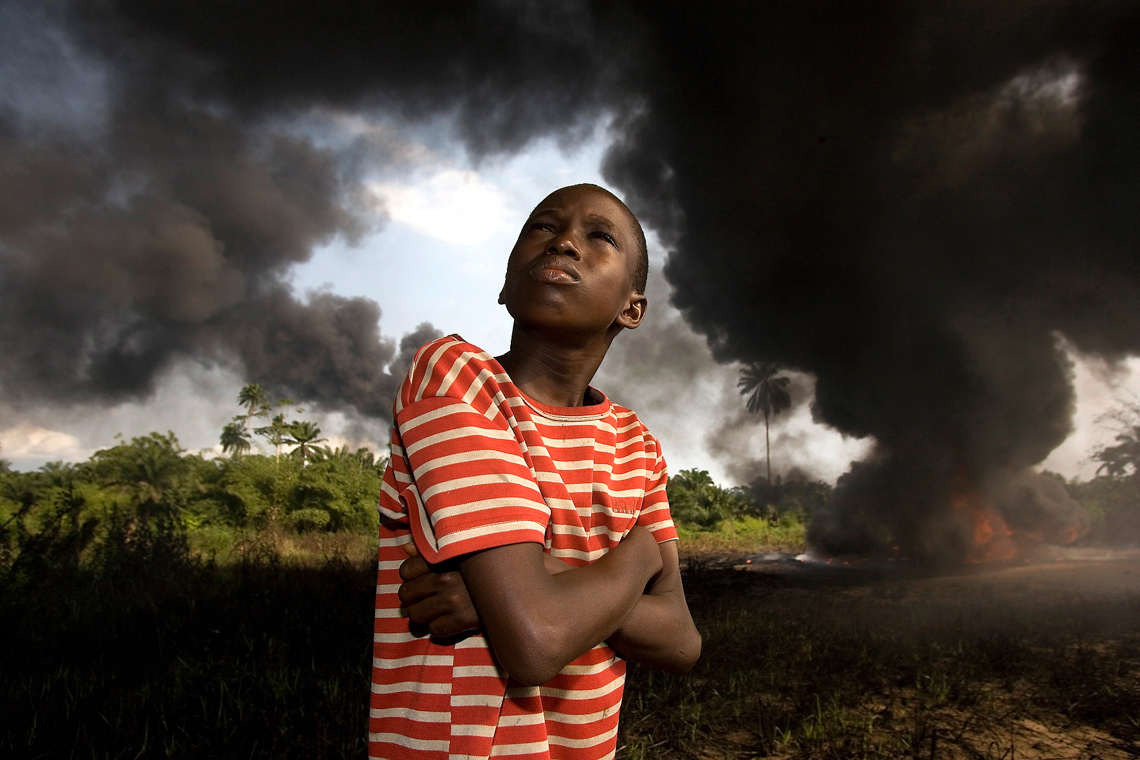 Portrait of boy wit h arms crossed, black smoke of oil in the background.