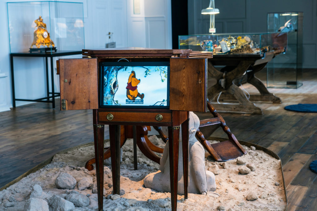 A screen showing a Winnie-the-Pooh-cartoon mounted in a cabinet. Exhibition interior in the background.