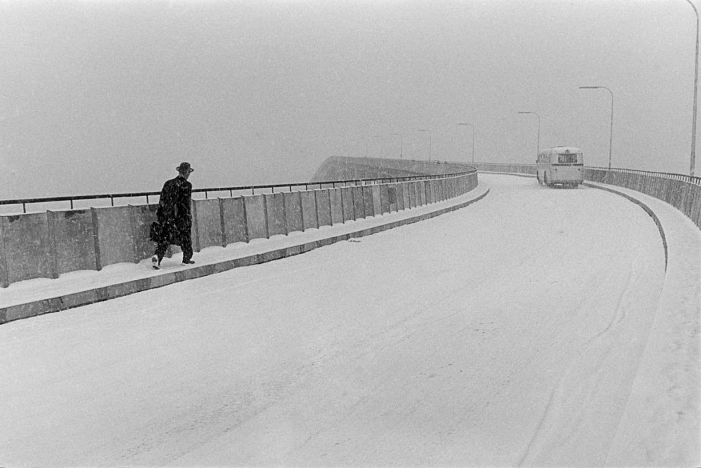 A man walking over a snow covered bridge. 